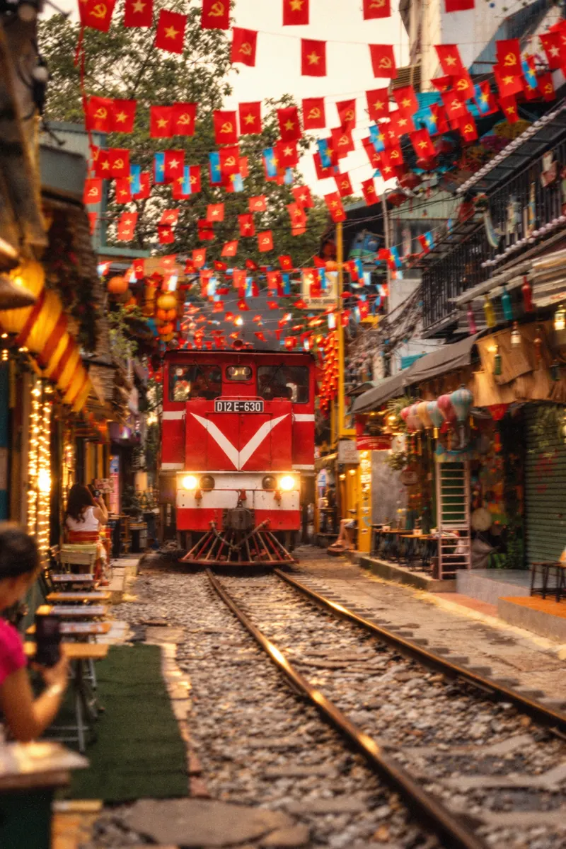Tren pasando entre casas y banderas en Hanói